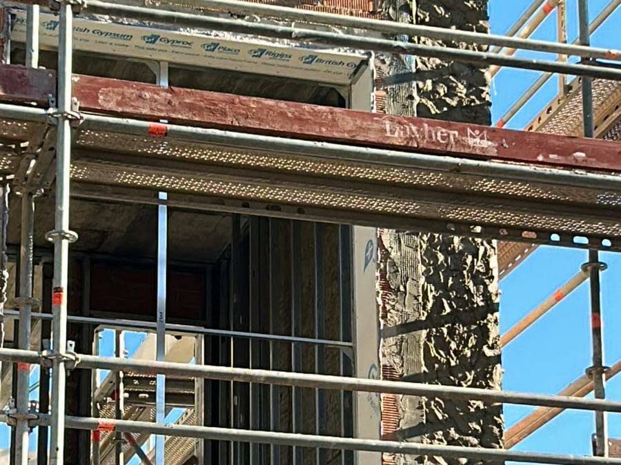 Fachada en obra con andamio, con la capa de mortero sobre el ladrillo