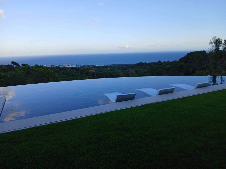 Vivienda unifamiliar terminada con piscina desbordante y jardín, con el mar al fondo